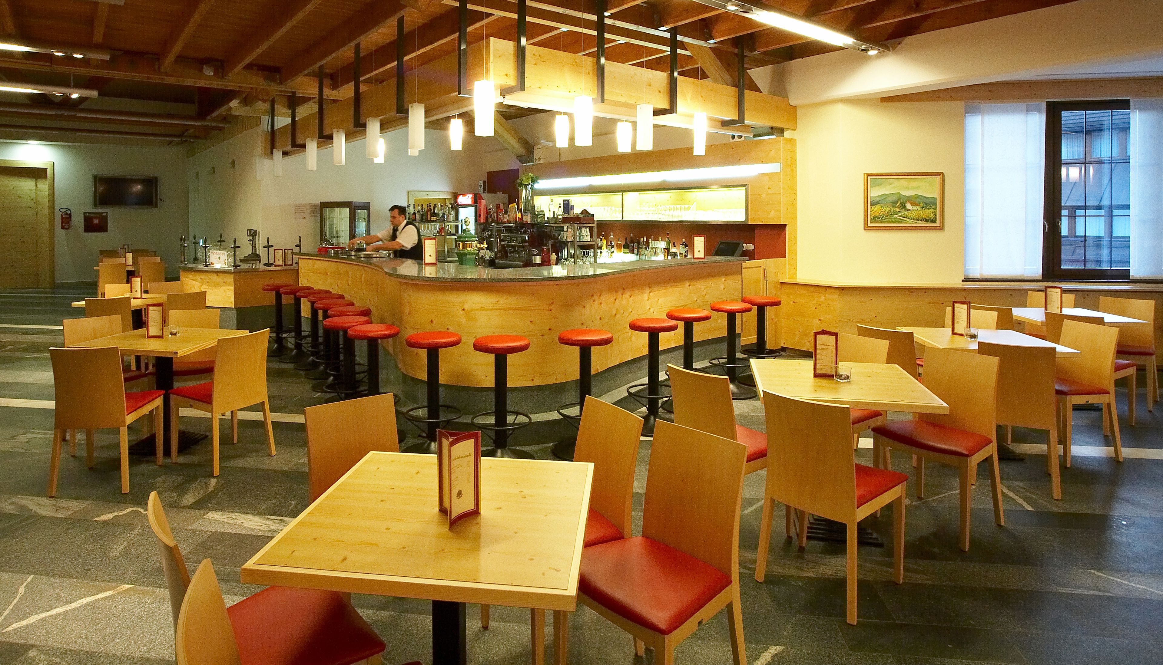 Un restaurant avec des tables en bois et des chaises rouges, un coin bar et des luminaires suspendus.