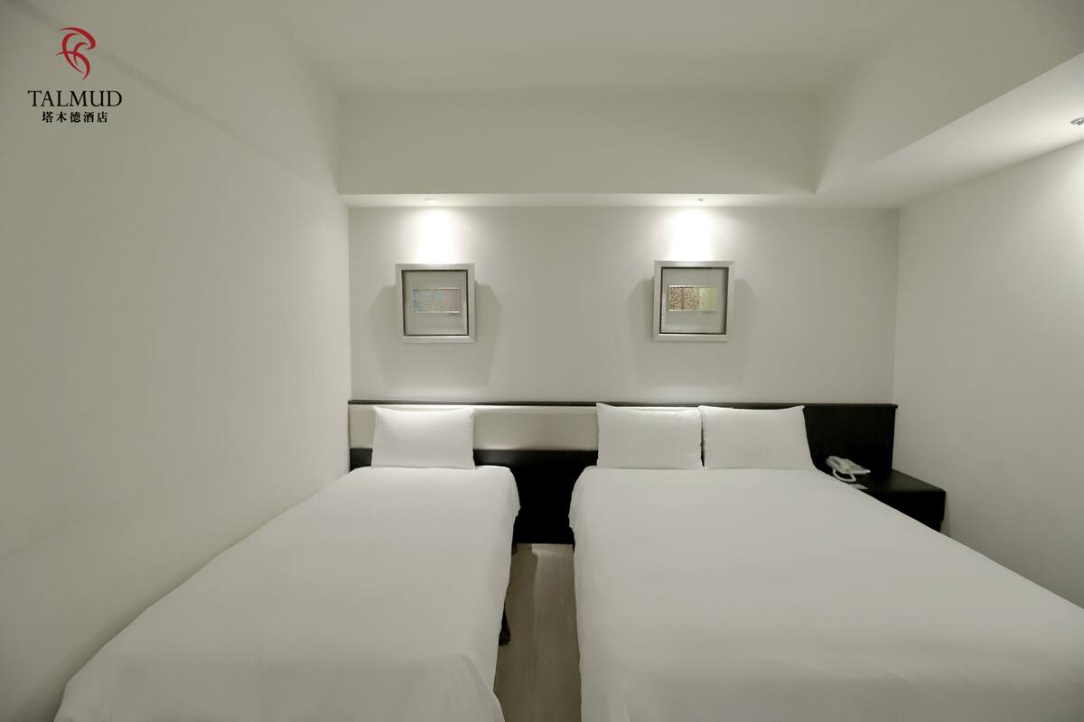 A hotel room with two beds, a nightstand with a phone, and framed pictures on the wall.