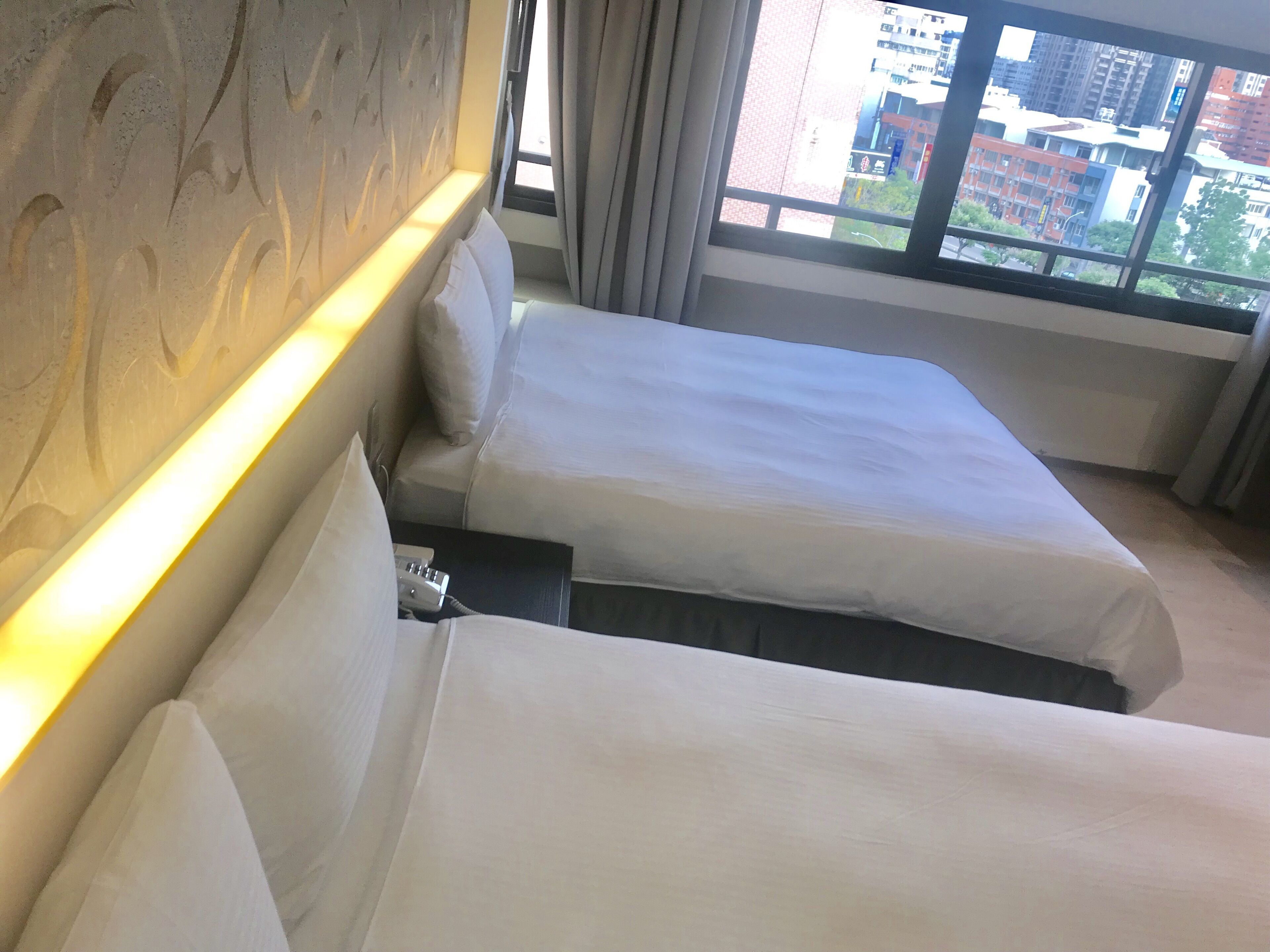 A hotel room with two beds, a headboard, and a window with a city view.