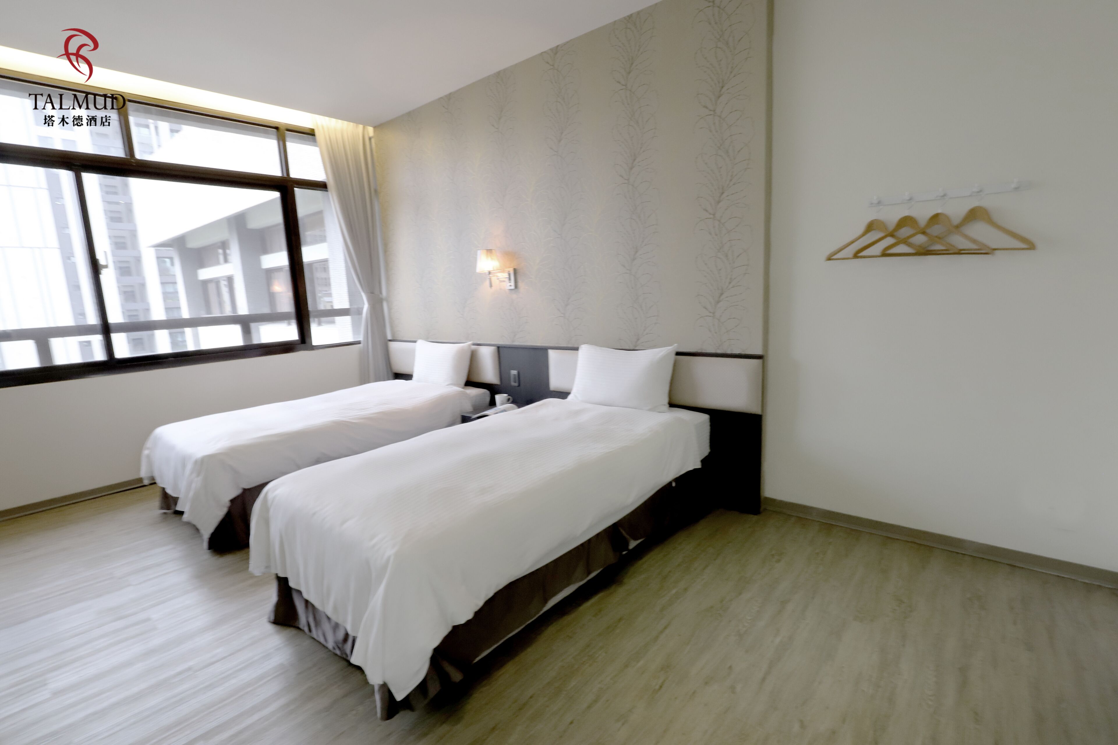 Habitación de hotel con dos camas, una ventana con cortinas, una lámpara de pared y un perchero.