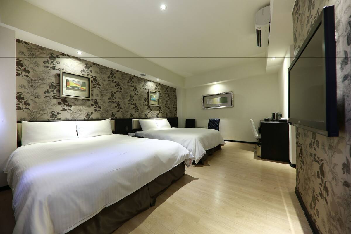 A hotel room with two beds, a TV, and a small kitchenette.