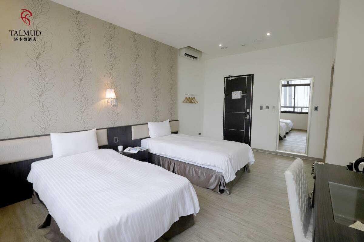 A hotel room with two beds, a desk, a mirror, and a wardrobe.