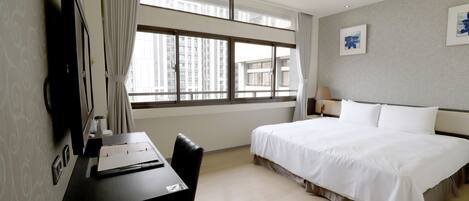 A hotel room with a large bed, a desk with a chair, a TV, and a window with curtains.