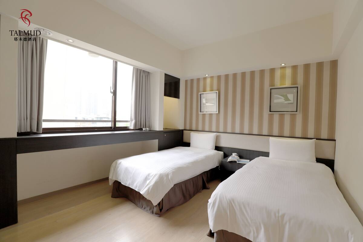 A hotel room with two beds, a large window, striped wallpaper, and a desk with a phone.