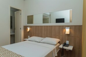 A hotel room with a bed, a bedside telephone, a mirror above the bed, and a door leading to a bathroom. - Golden Suite Hotel (Campinas)