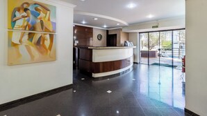 A hotel reception area with a curved reception desk, a large abstract painting on the wall, and a glass door leading outside.