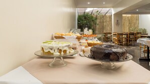 A buffet with various desserts on display, including cakes and pastries, in a modern dining area with wooden tables and chairs.