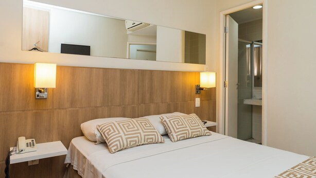 A hotel room with a wooden headboard, two bedside lamps, a telephone, and a mirror above the bed.