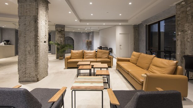 A spacious living area with a large sofa set, multiple tables, and a stone pillar. - Sparrow Hotel (Taichung)