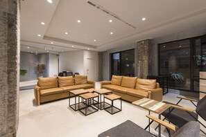 Una sala de estar moderna con un sofá grande en forma de L, dos mesas de centro de madera y una alfombra gris.