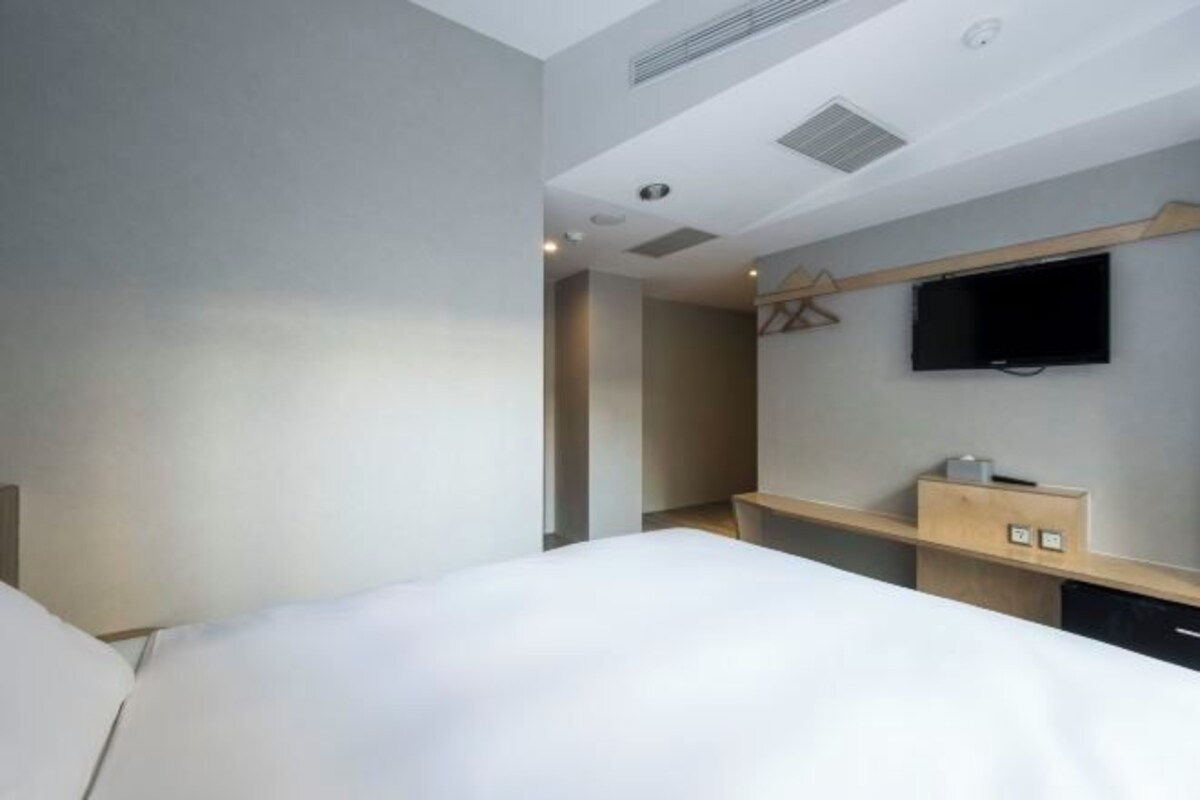 Ein modernes Hotelzimmer mit einem großen Bett, einem flachbildfernseher an der Wand und einem Holztisch mit Stuhl.