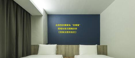 A hotel room with two beds, a small wooden table, and a dark blue accent wall.