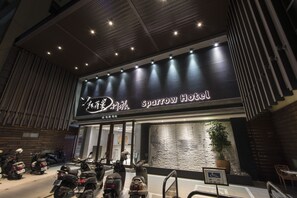 El exterior del Hotel Sparrow, con un diseño moderno, presenta un letrero llamativo y una fila de scooters estacionados afuera.