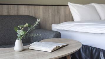A neatly arranged hotel room with a round wooden table, a white vase with a plant, and a bed with white linens.