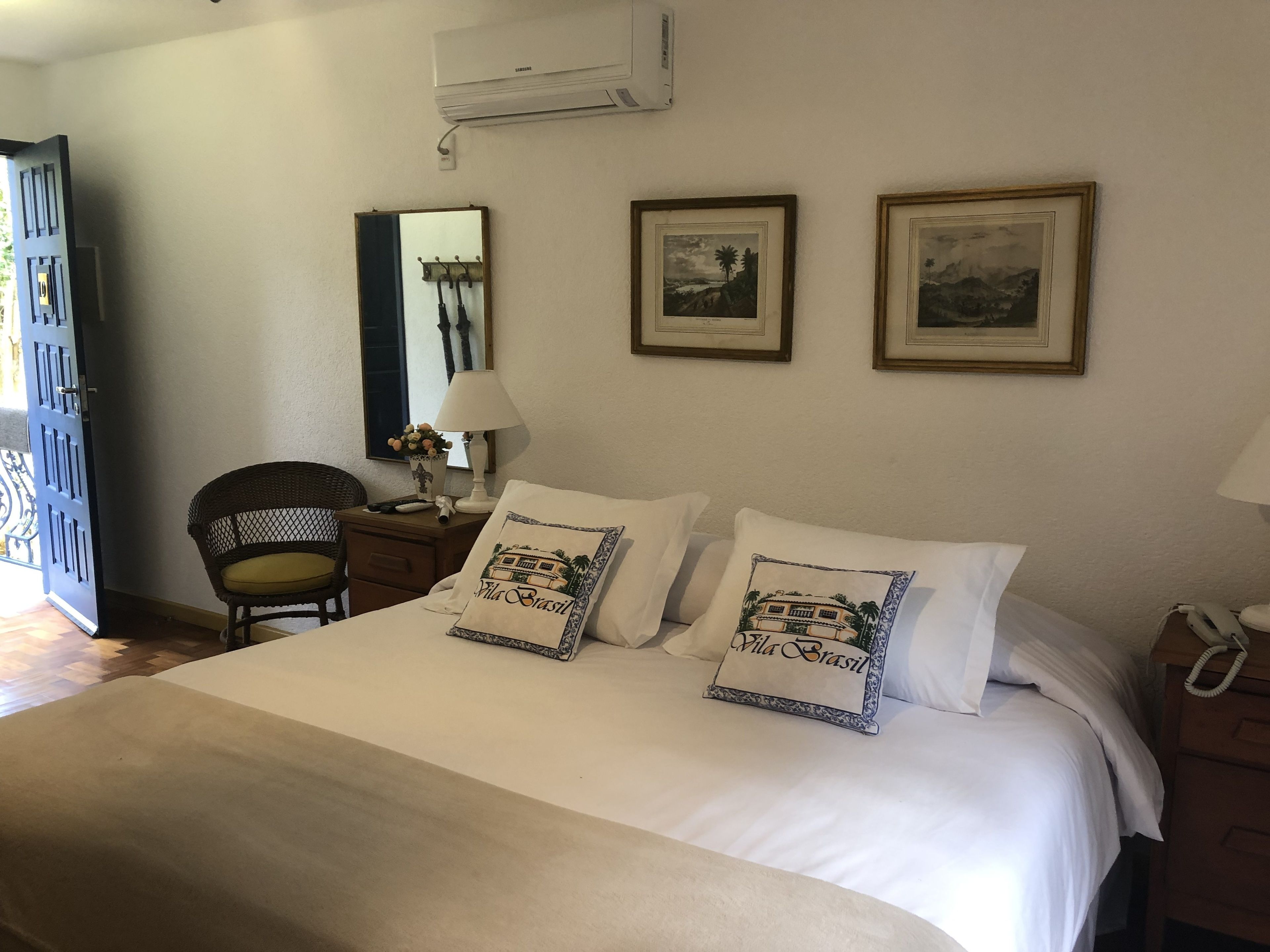 A neatly made bed with two pillows, a bedside lamp, a chair, and a wall-mounted air conditioner.