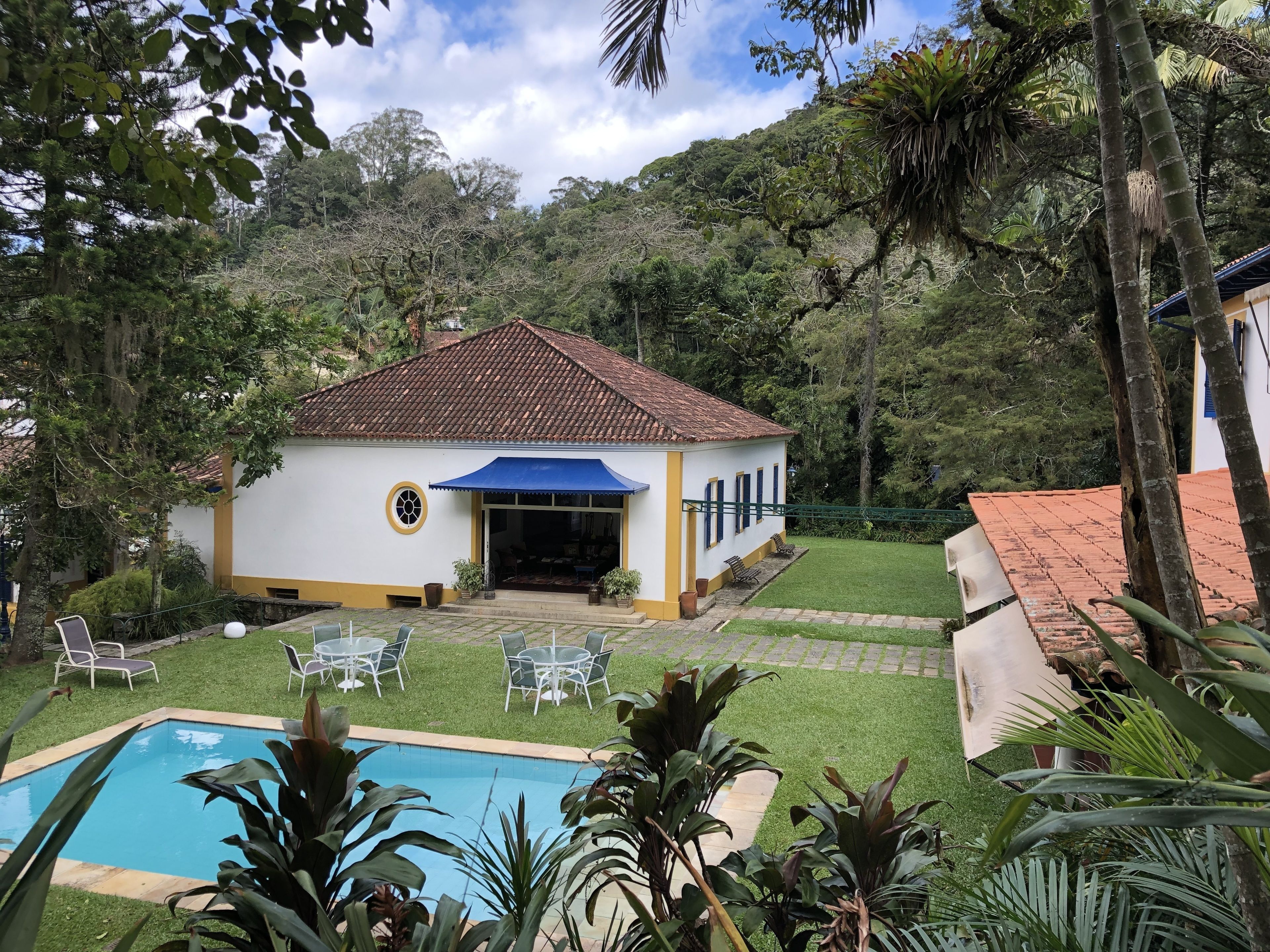 A white building with a tiled roof, a pool, and a patio area with chairs and tables.