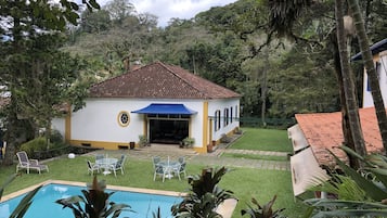 A white building with a tiled roof, a pool, and a patio area with chairs and tables.