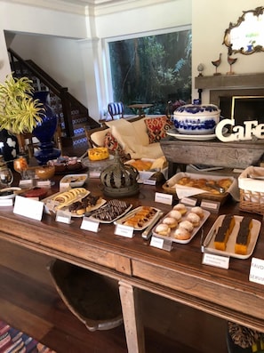 A buffet table with various pastries and desserts labeled in a hotel setting. - Pousada Vila Brasil (Petrópolis)