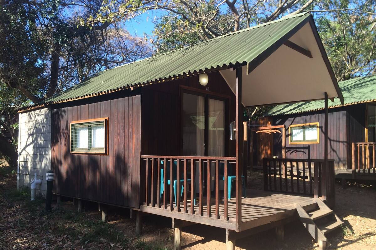 Une cabane en bois dotée d’une véranda, de grandes fenêtres et d’un toit en métal.
