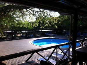 A pool area with a wooden deck, lounge chairs, and a covered seating area.