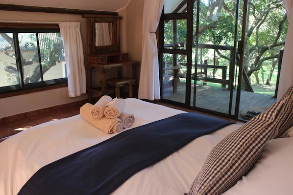 A bedroom with a large bed, a wooden desk, and a view of an outdoor deck.