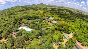 An aerial view of a resort with multiple buildings surrounded by dense greenery and hills in the background.