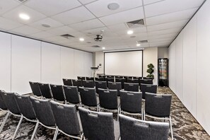 Un salón de conferencias con filas de sillas, un proyector y una pantalla.