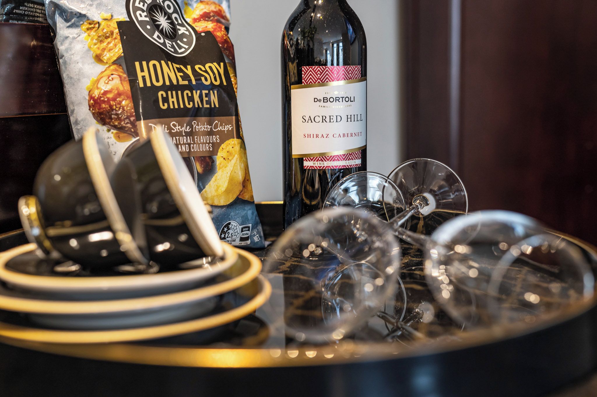 Une table avec un paquet de chips au poulet, sauce soja et miel, une bouteille de vin et plusieurs verres à vin.