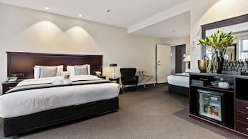 A hotel room with a large bed, a smaller bed, a desk with a refrigerator, a chair, and a mirror.