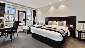 A modern hotel room with a large bed, a desk, a chair, and a window with a view of bare trees. - International Hotel Wagga Wagga (East Wagga Wagga)