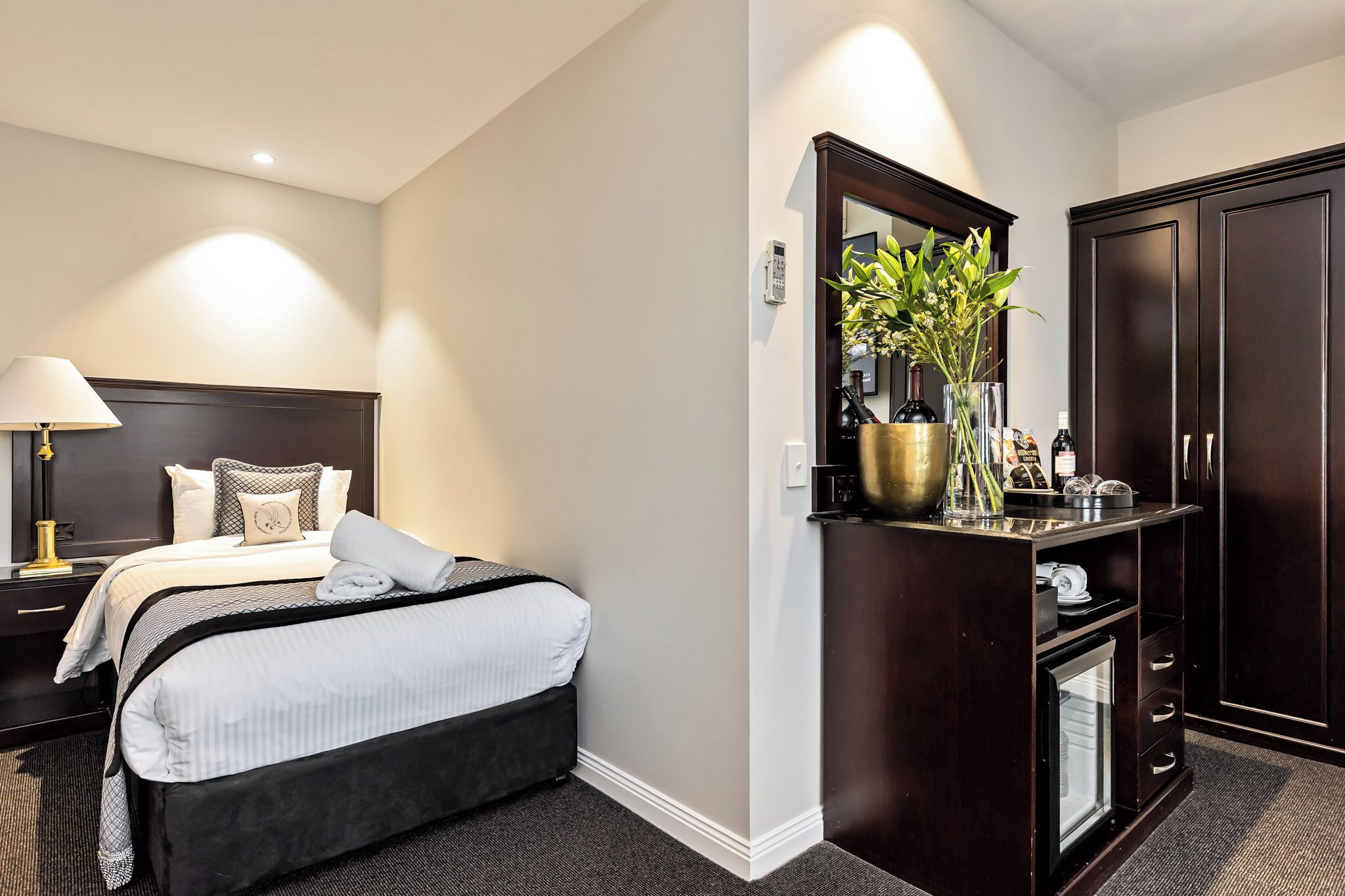 Ein Hotelzimmer mit Bett, Nachttisch, Lampe, Schminktisch und kleinem Kühlschrank.