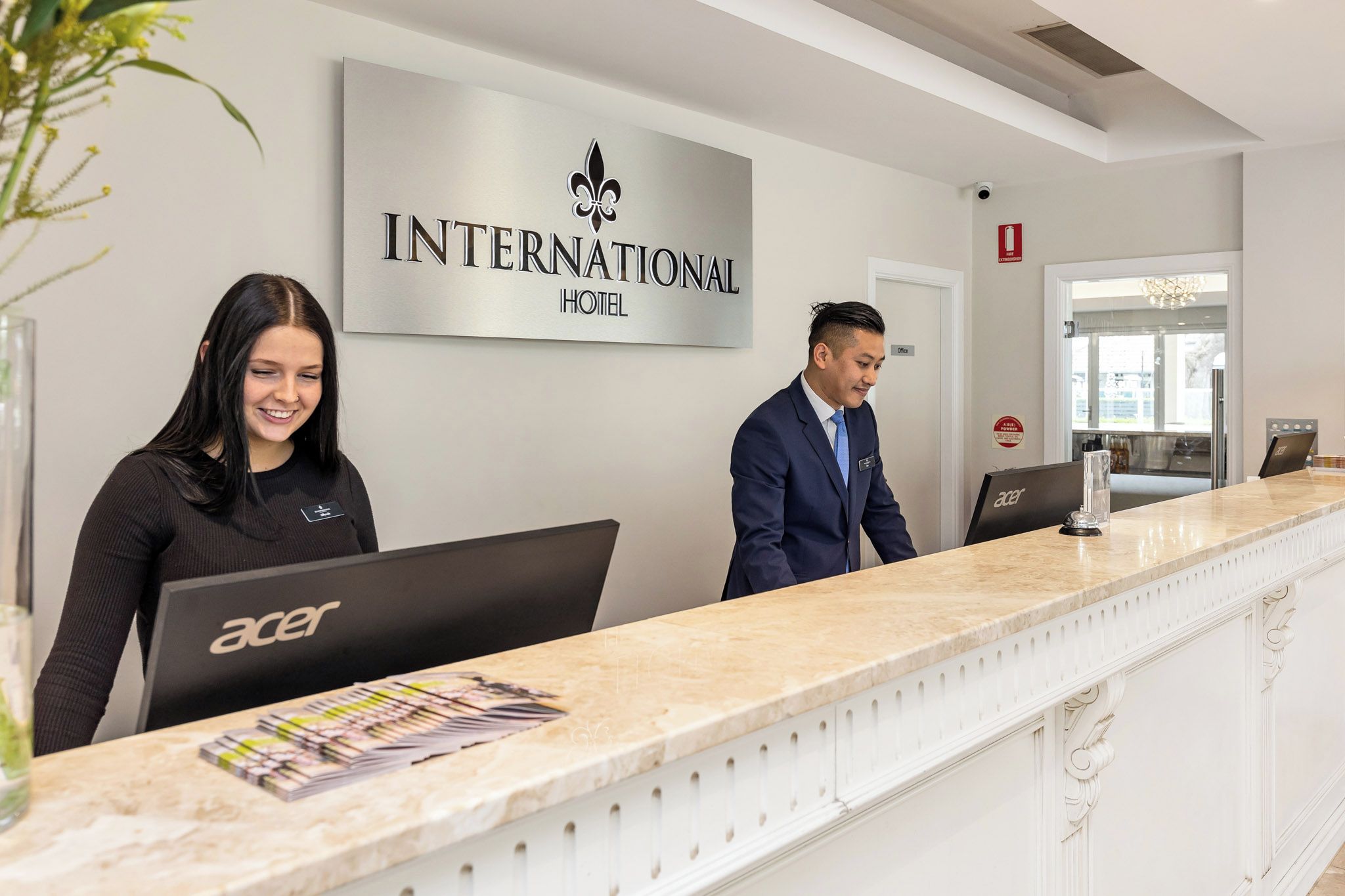 A reception desk at the INTERNATIONAL HOTEL with a modern design, a sign above indicating the hotel name, and a computer on the desk.