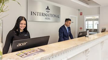 A reception desk at the INTERNATIONAL HOTEL with a modern design, a sign above indicating the hotel name, and a computer on the desk.