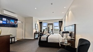 A modern hotel room with a large bed, a desk, a flat-screen TV, and a view of the outdoors through the windows. - International Hotel Wagga Wagga (East Wagga Wagga)