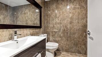 Een moderne badkamer met een ruime wastafel, toilet en marmeren wanden.