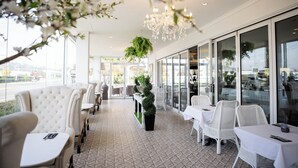 A restaurant with white upholstered chairs and tables, a patterned floor, and a hanging plant. - International Hotel Wagga Wagga (East Wagga Wagga)