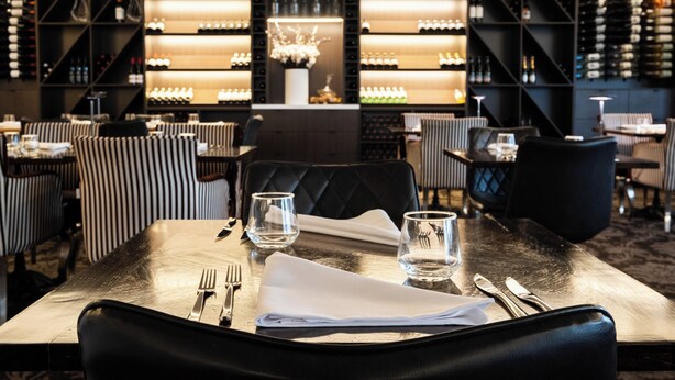 A restaurant with a modern interior, featuring striped chairs, a central dining table with a white napkin, and a wine rack in the background. - International Hotel Wagga Wagga (East Wagga Wagga)