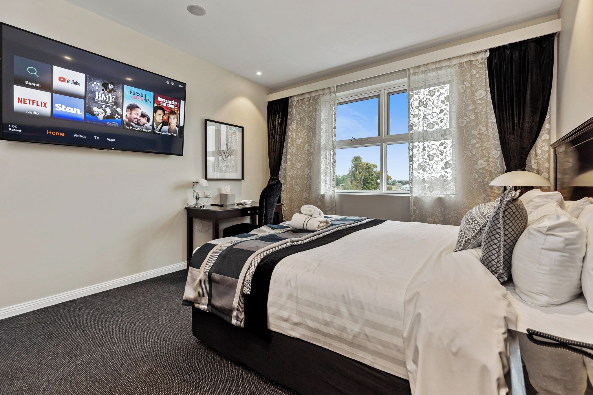Habitación de hotel con cama, escritorio, televisión en la pared y ventana con cortinas.