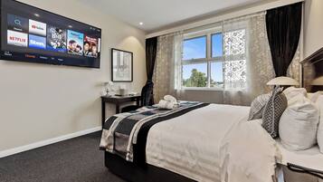A hotel room with a bed, a desk, a TV mounted on the wall, and a window with curtains.