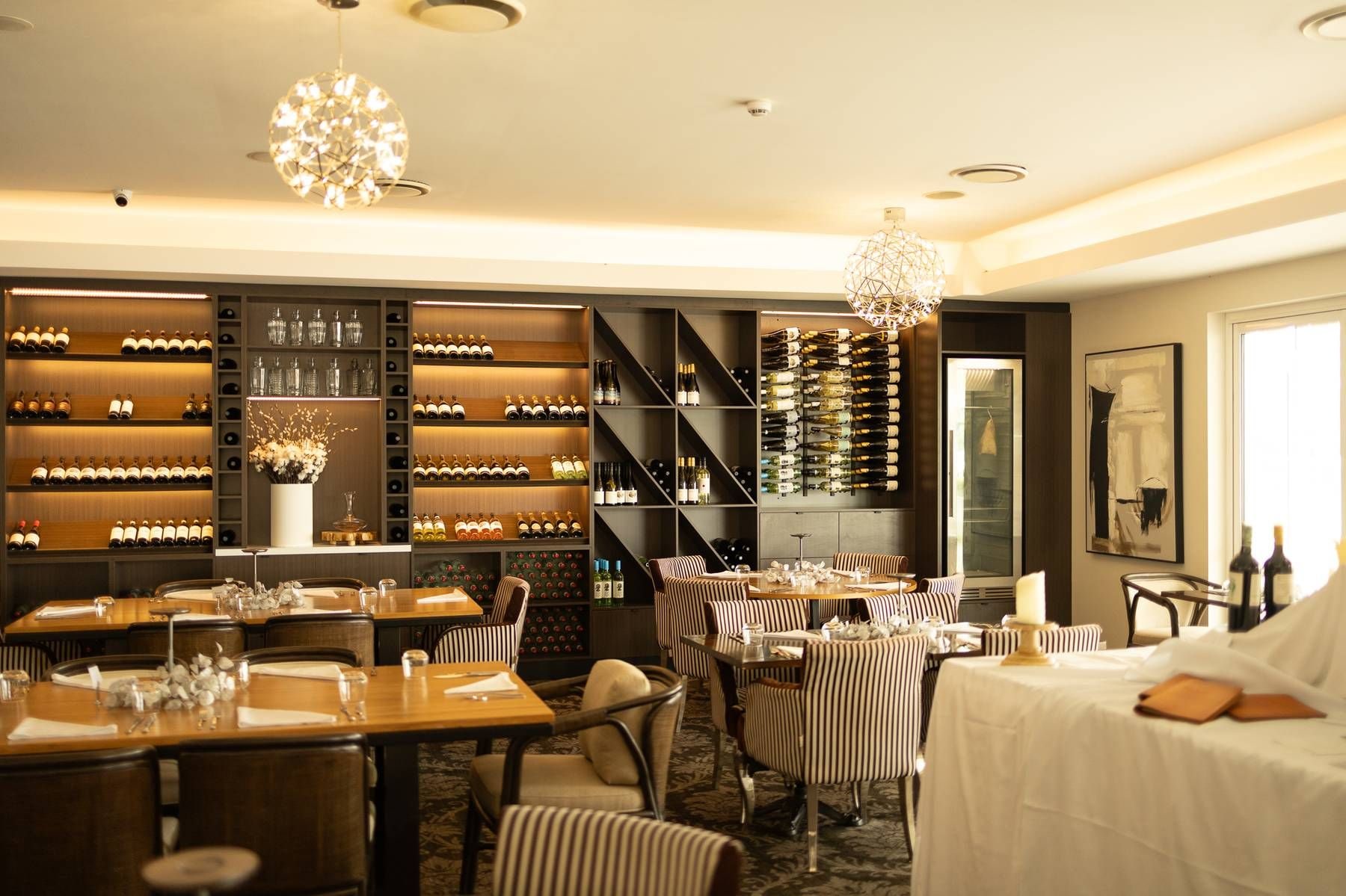 A restaurant with multiple dining tables, chairs, and a wine cellar with numerous bottles.