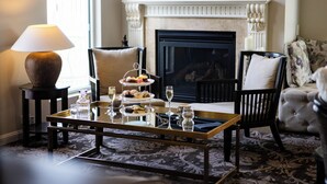A cozy living room with a fireplace, a coffee table with a tray of pastries, a lamp, and a television mounted on the wall. - International Hotel Wagga Wagga (East Wagga Wagga)