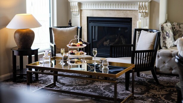 A cozy living room with a fireplace, a coffee table with a tray of pastries, a lamp, and a television mounted on the wall. - International Hotel Wagga Wagga (East Wagga Wagga)