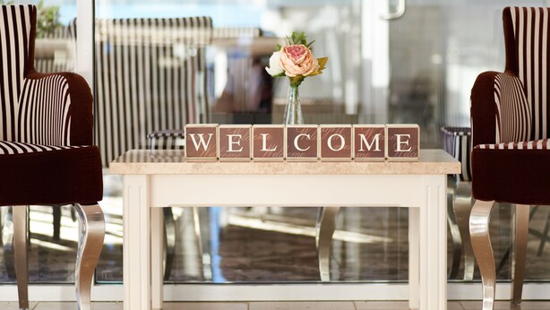 A reception desk with a 'WELCOME' sign and a vase with a flower. - International Hotel Wagga Wagga (East Wagga Wagga)