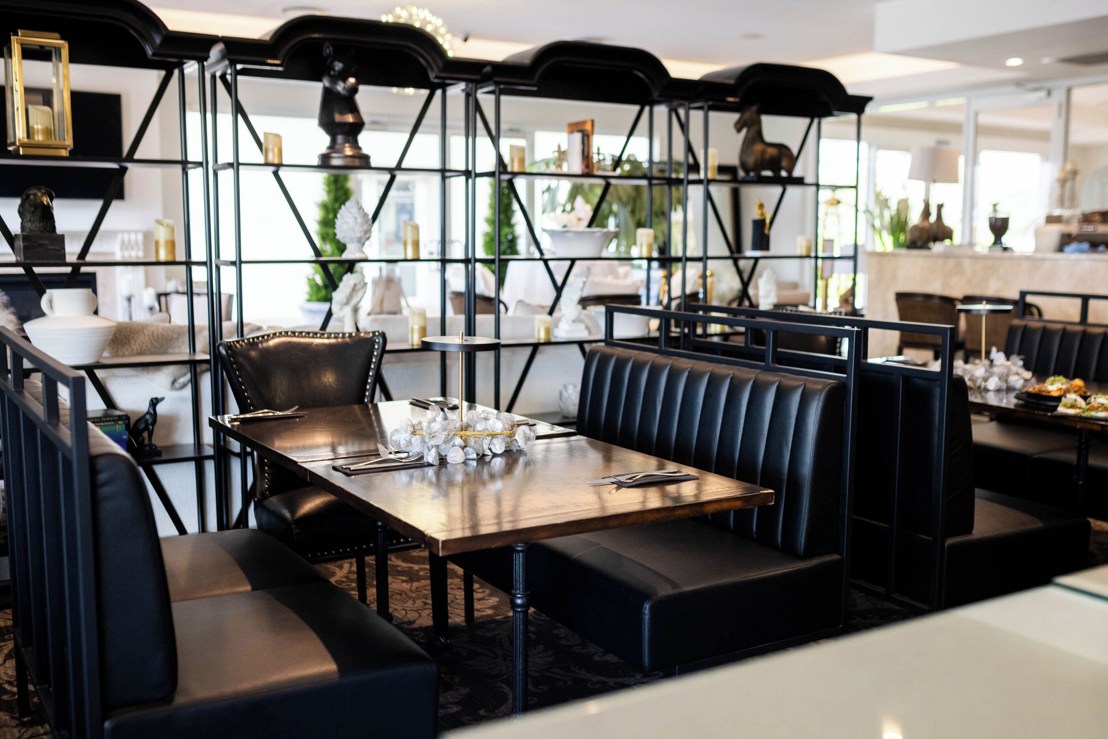 A restaurant with black leather booths and a wooden table set for dining.
