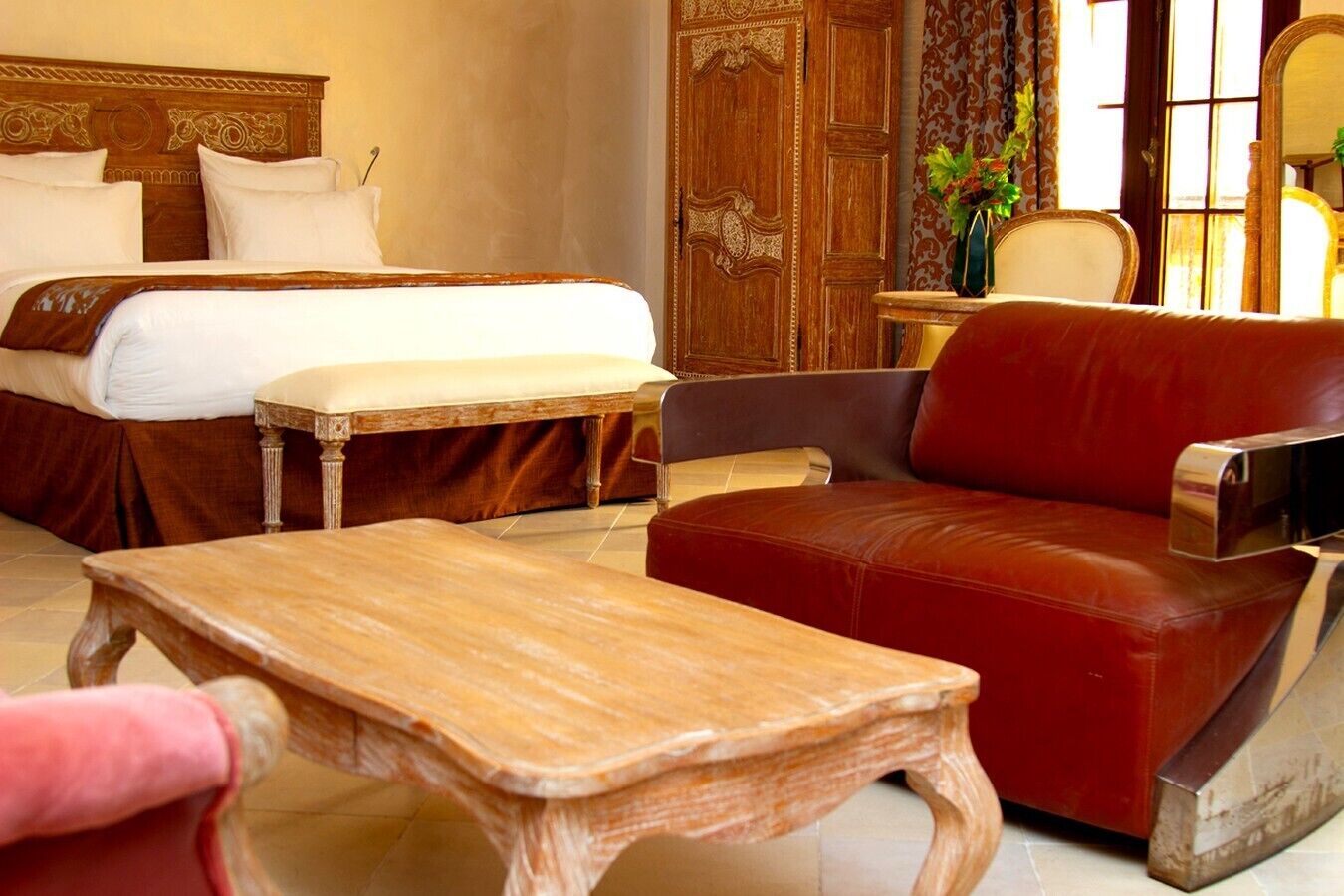 A hotel room with a bed, a wooden table, a red leather sofa, and a mirror.