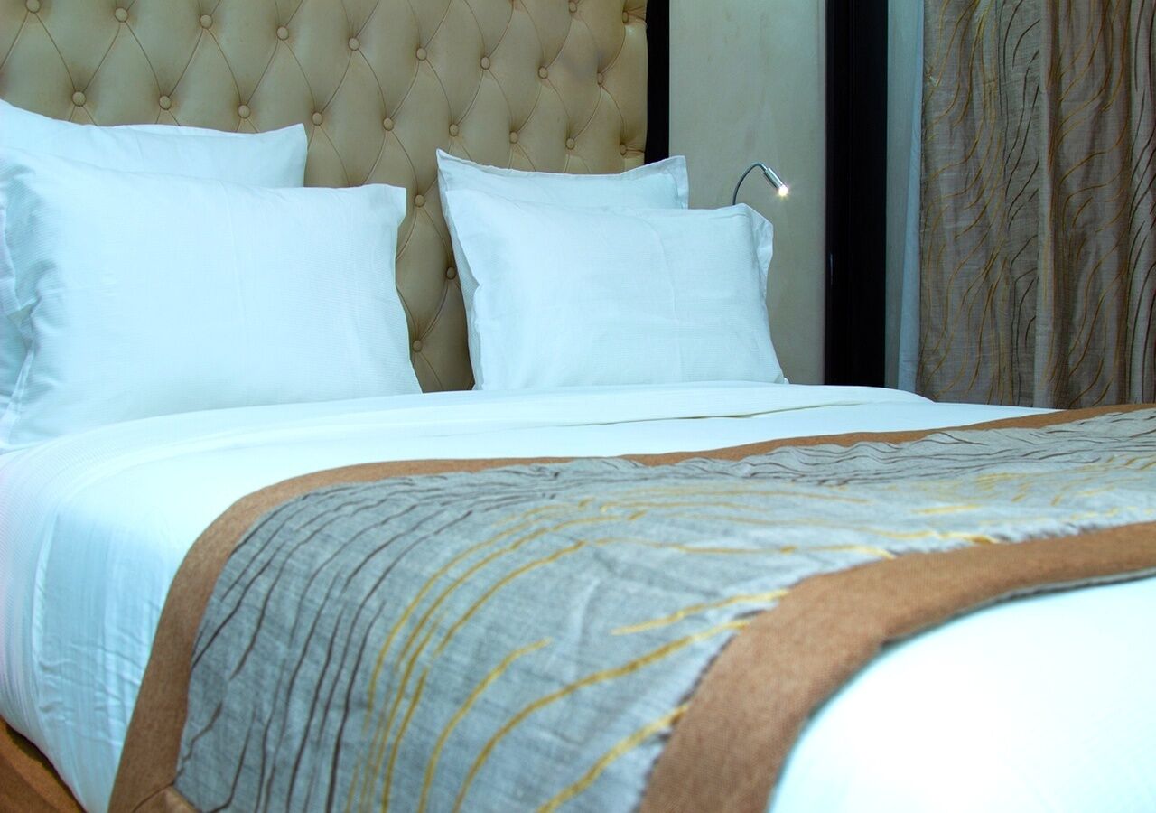 A neatly made bed with a tufted headboard, white bedding, and a patterned throw blanket.