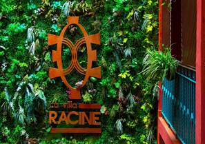 A sign with a logo and the text "La villa RACINE" against a backdrop of lush green foliage. - Hotel La Villa Racine (Dakar)
