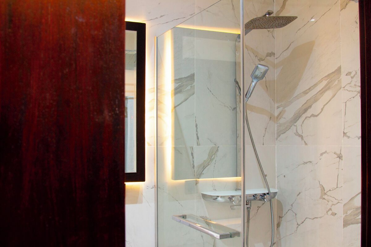 A modern bathroom with a glass-enclosed shower, marble walls, and a wooden door.