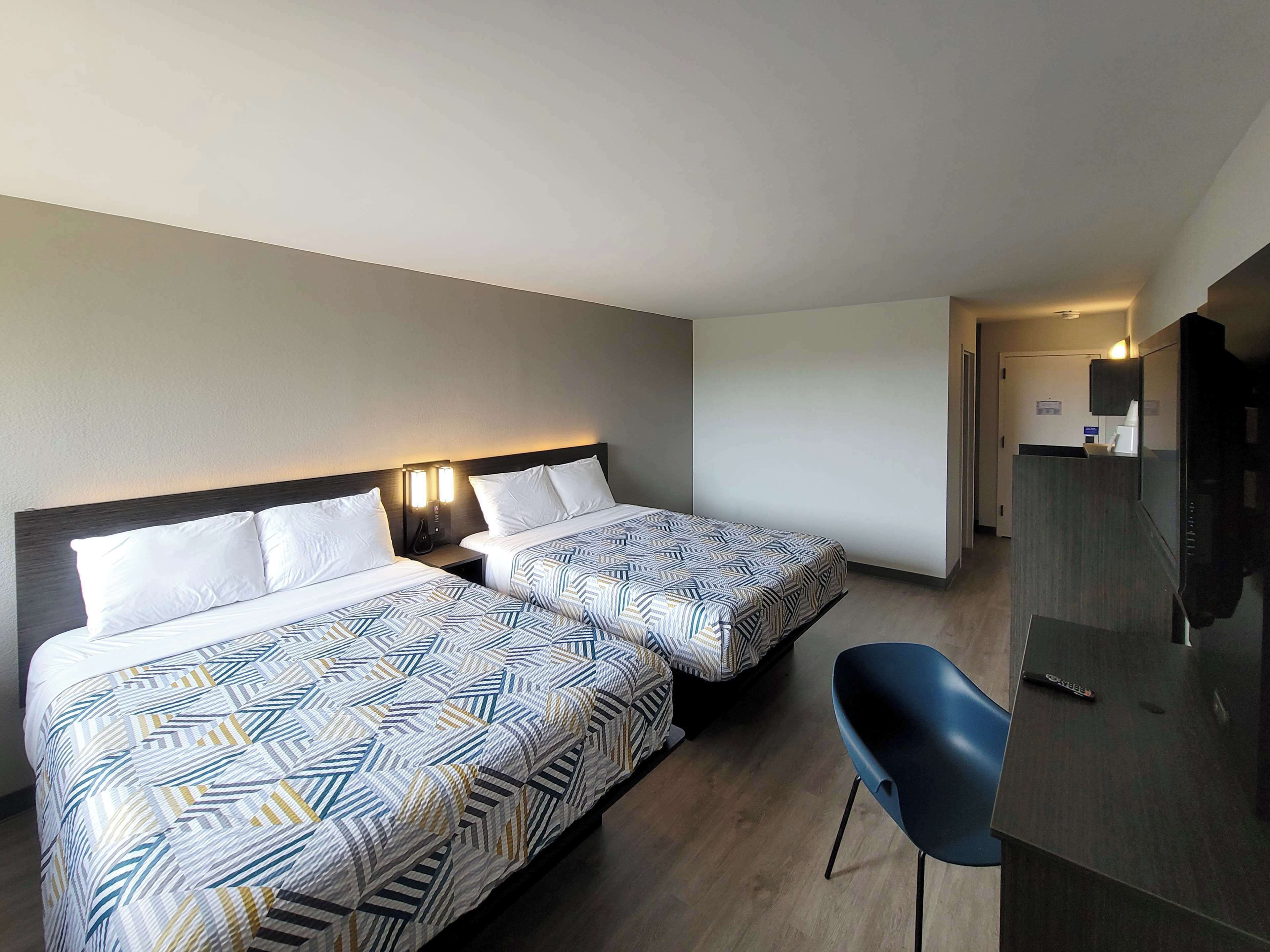 A hotel room with two beds, a desk, a chair, and a TV.