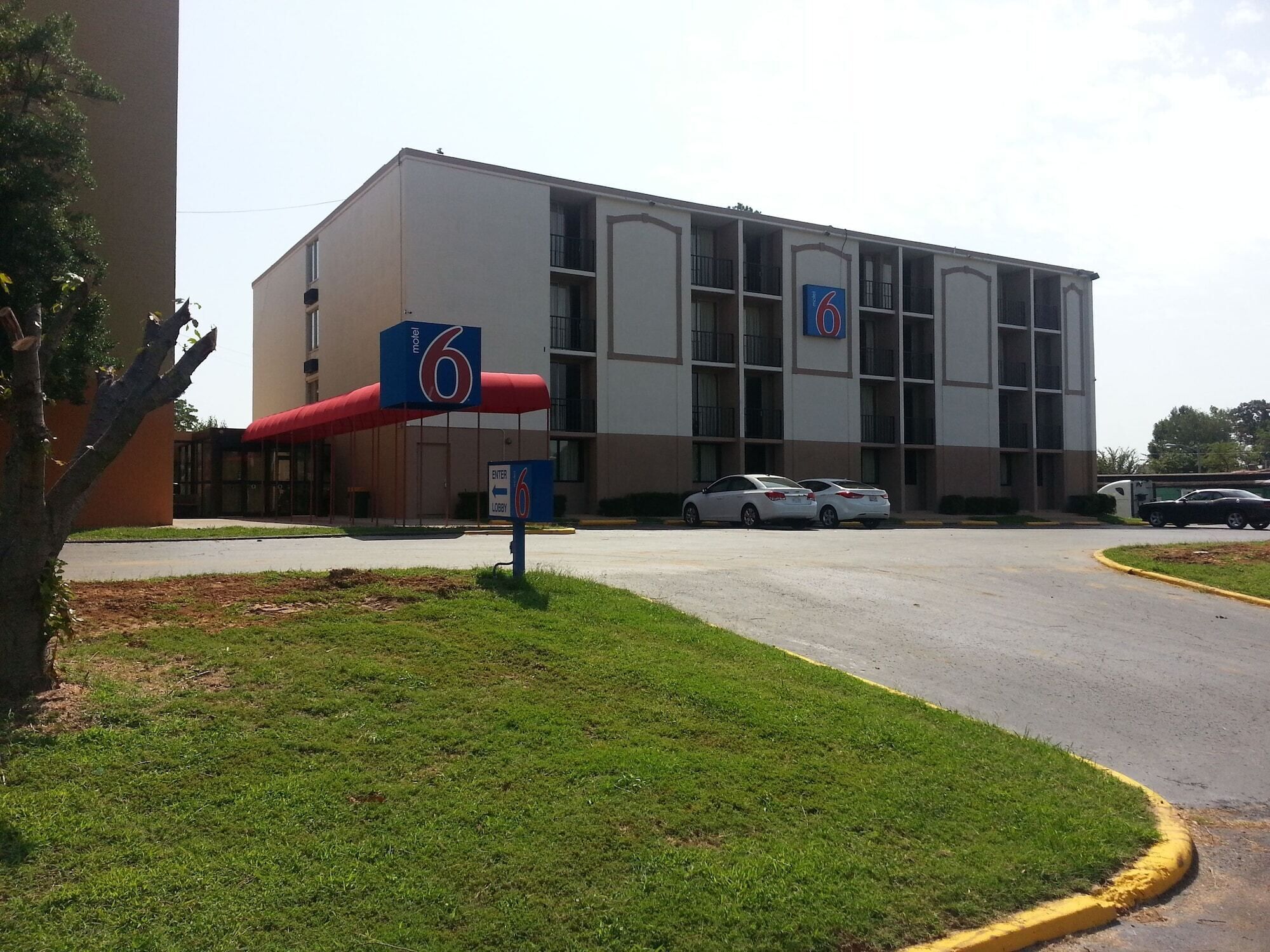 A motel with a large building, multiple balconies, and a parking area with cars.
